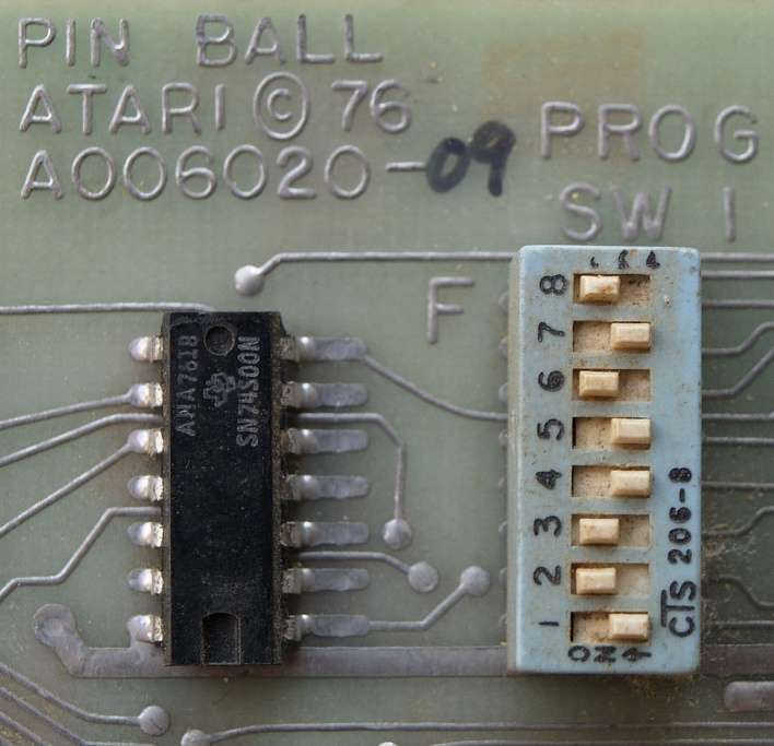 A blue eight-position DIP switch soldered onto an old green circuit board, some switches pushed one way and some the other