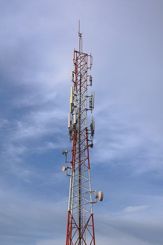 A tall red-and-white mobile phone mast carrying many antennas against a blue sky