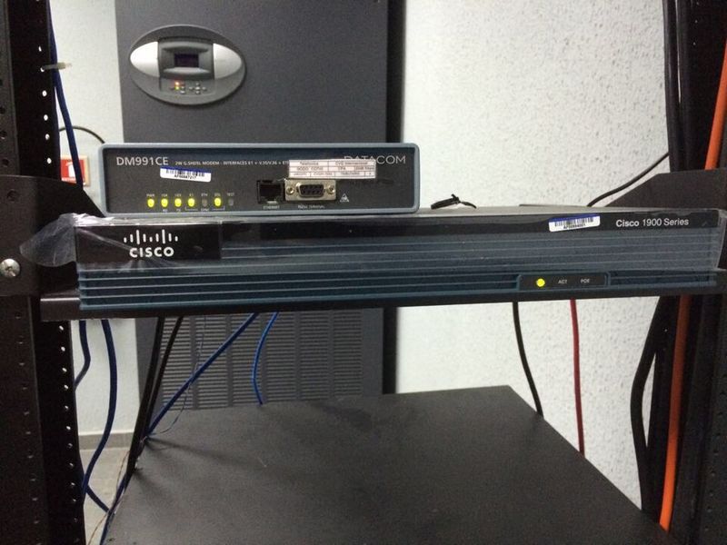 A rack-mounted network router with status lights, installed in an equipment cabinet below a modem