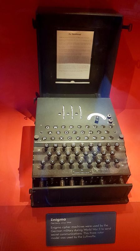An Enigma cipher machine in a museum case, with its keyboard, lamp board and rotors visible