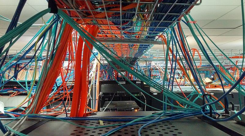 Hundreds of blue, orange and green network cables running through ceiling trays above computer racks