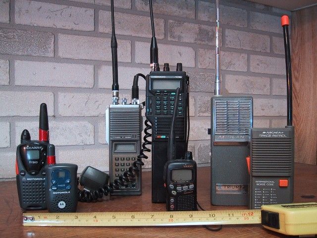 A row of handheld walkie-talkie radios of different sizes standing on a shelf