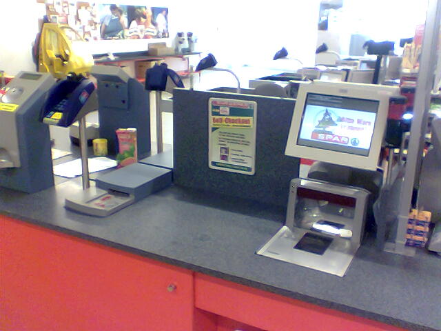 A supermarket self-checkout with a flatbed barcode scanner window, a touch screen and a card payment terminal