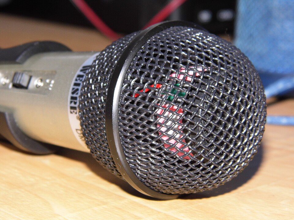 Close-up of a handheld microphone with a round metal mesh grille over the diaphragm