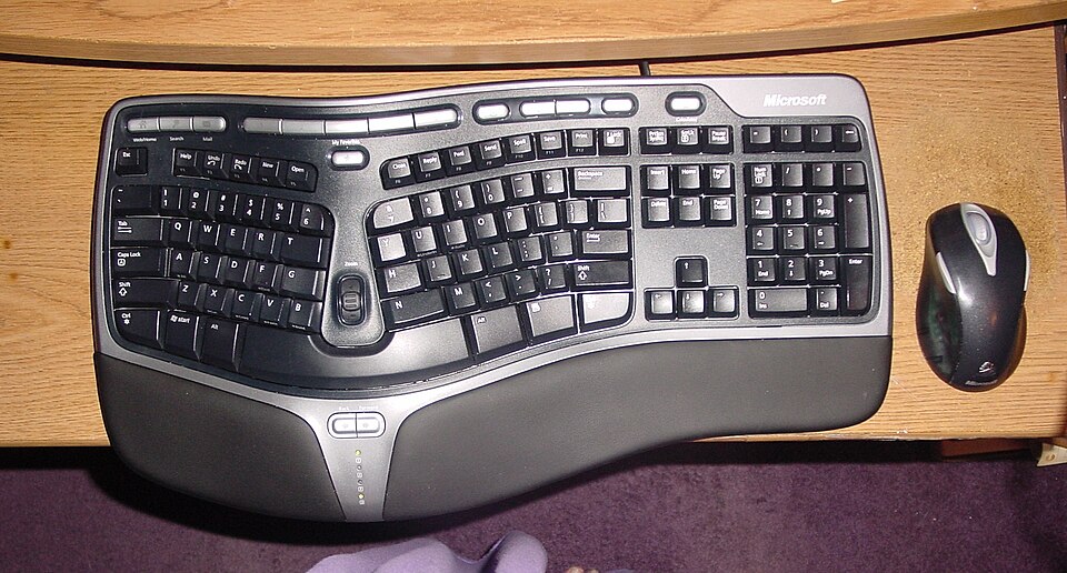 A split, curved ergonomic keyboard with a padded palm rest, next to a wireless mouse on a desk