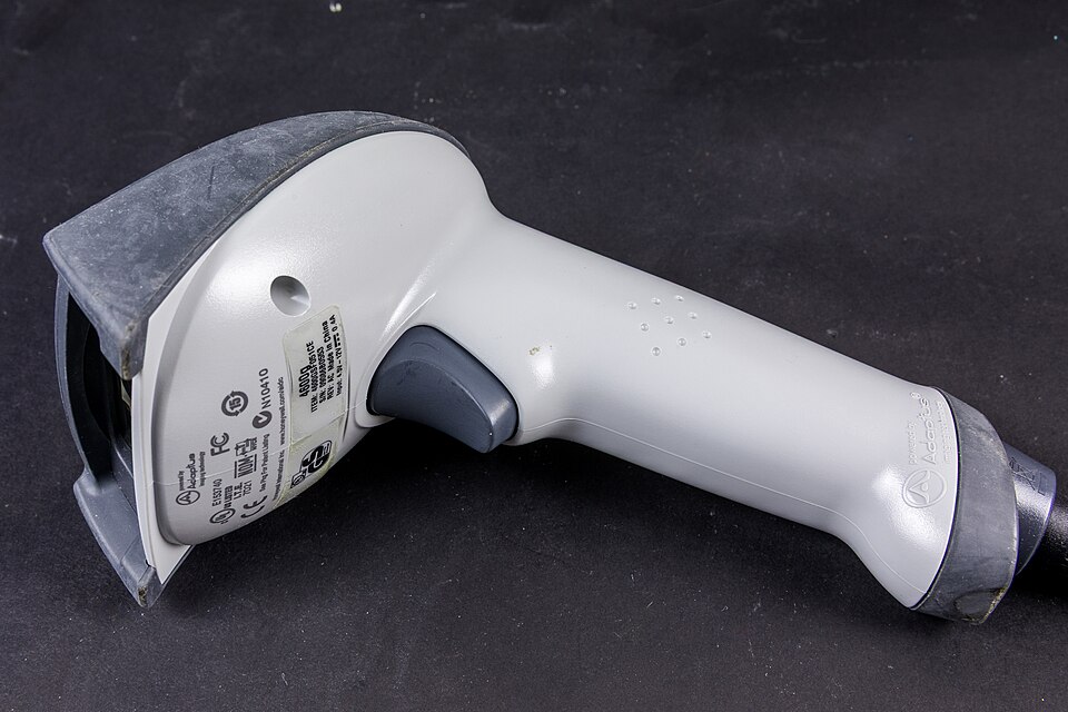A white handheld barcode scanner with a trigger, lying on a dark surface