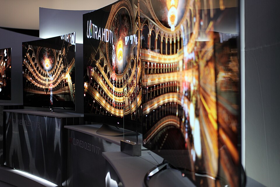 A row of large curved OLED televisions on display at a trade show
