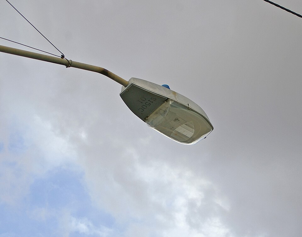 A street lamp on a pole with a small blue light sensor cap on top of the lamp head
