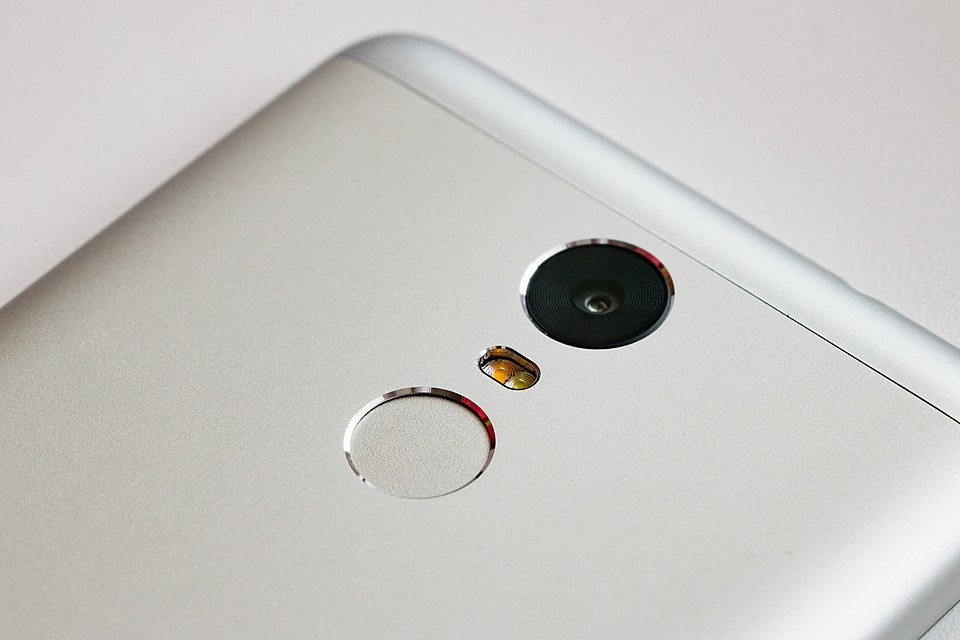 The round fingerprint sensor below the camera on the back of a silver smartphone