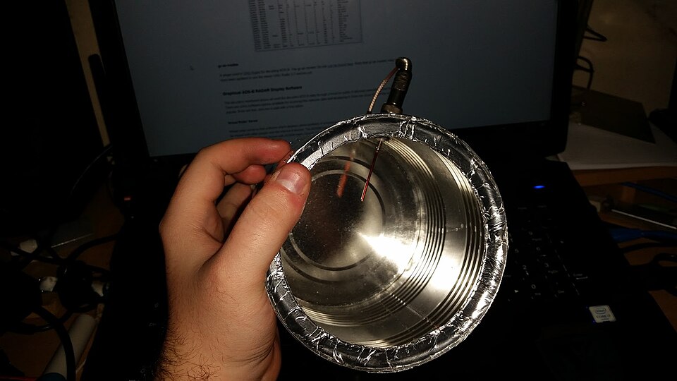 A hand holding a home-made tin-can Wi-Fi antenna in front of a laptop