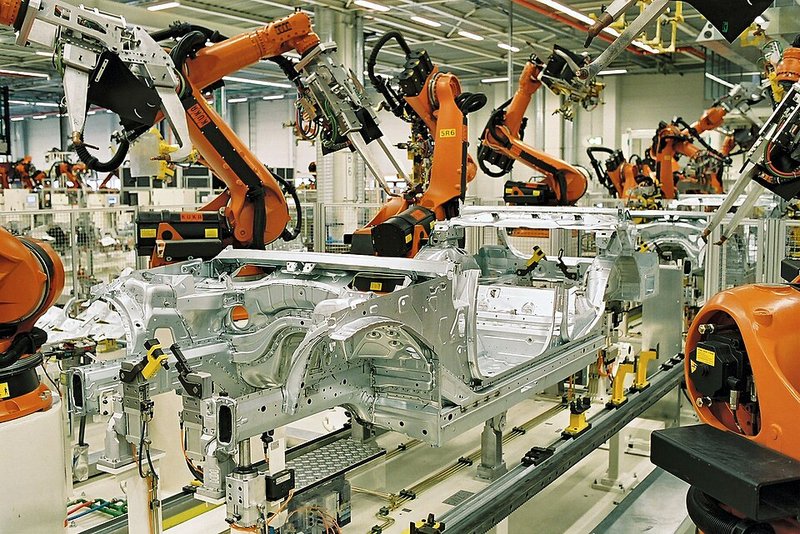 Rows of orange industrial robot arms welding car body shells on a factory production line