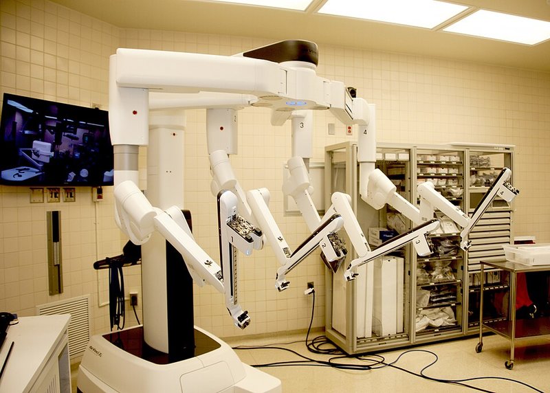 A surgical robot with four white jointed arms standing over an operating table in a hospital theatre