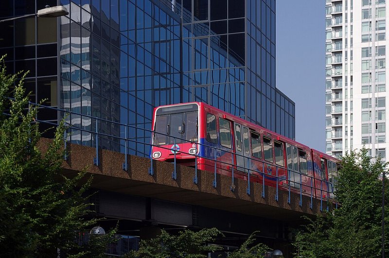 A red and blue light-railway train crossing an elevated track between office towers