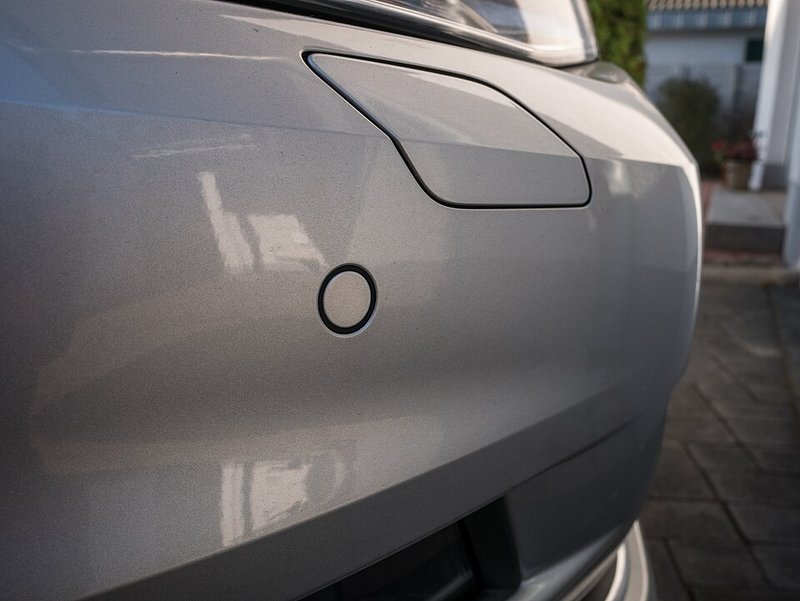 Close-up of a round parking sensor set into the painted bumper of a car
