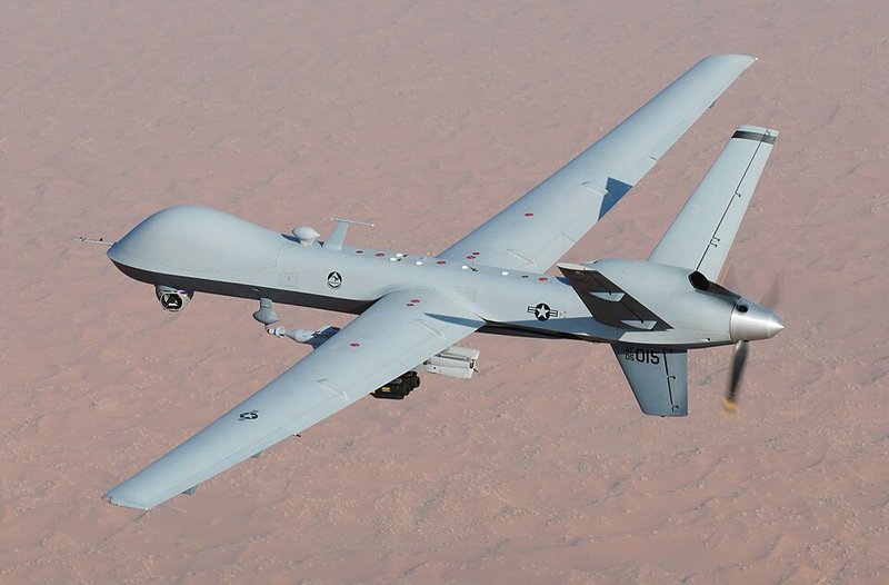 A large grey unmanned aircraft flying over a desert