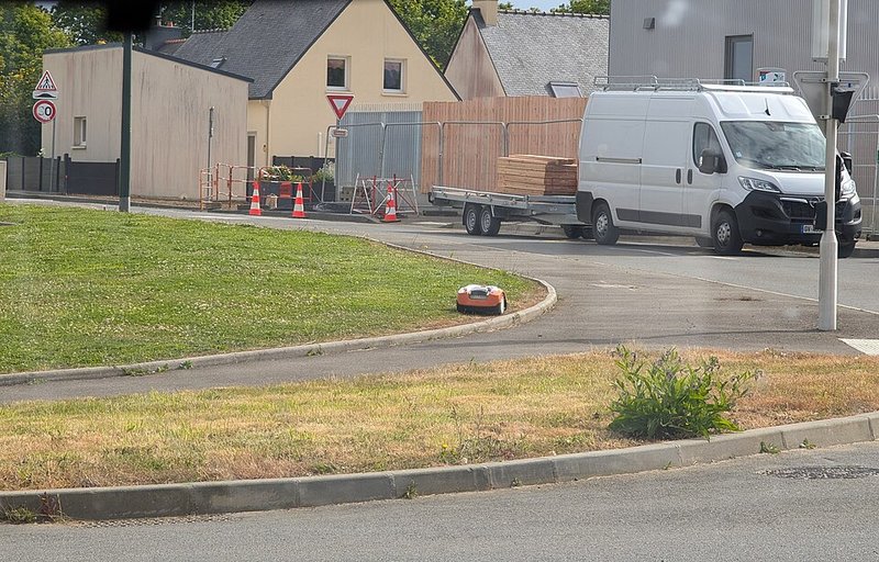 A small robot lawn mower cutting the grass on a roundabout beside a road