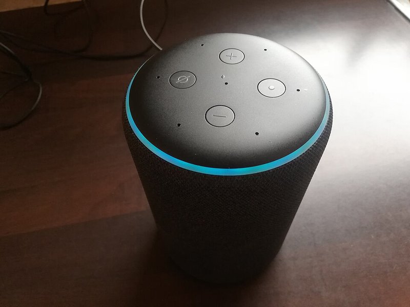 A cylindrical smart speaker on a table with a glowing blue ring on top