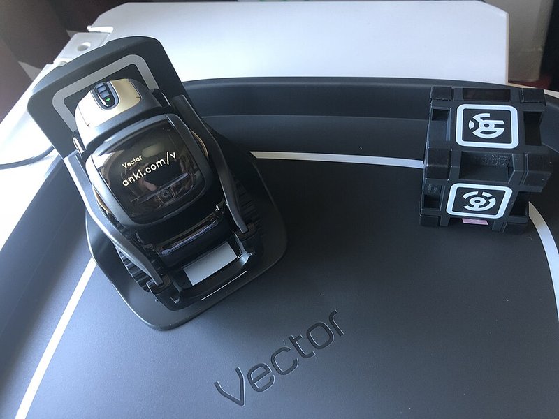 A small dark personal-assistant robot with a face screen, sitting in its packaging