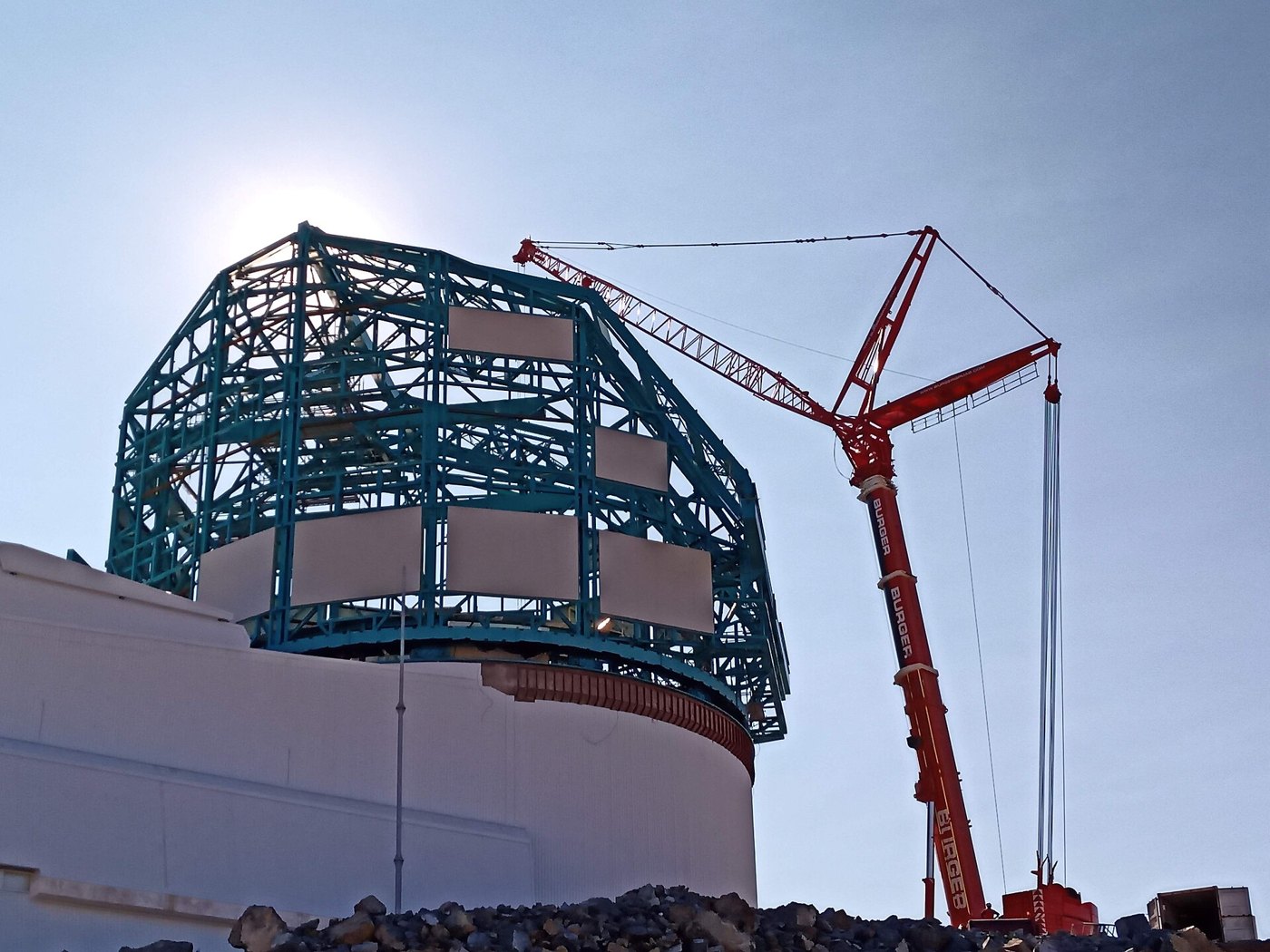 A very large mobile crane on a construction site, its jib raised and hook block hanging on multiple rope falls.