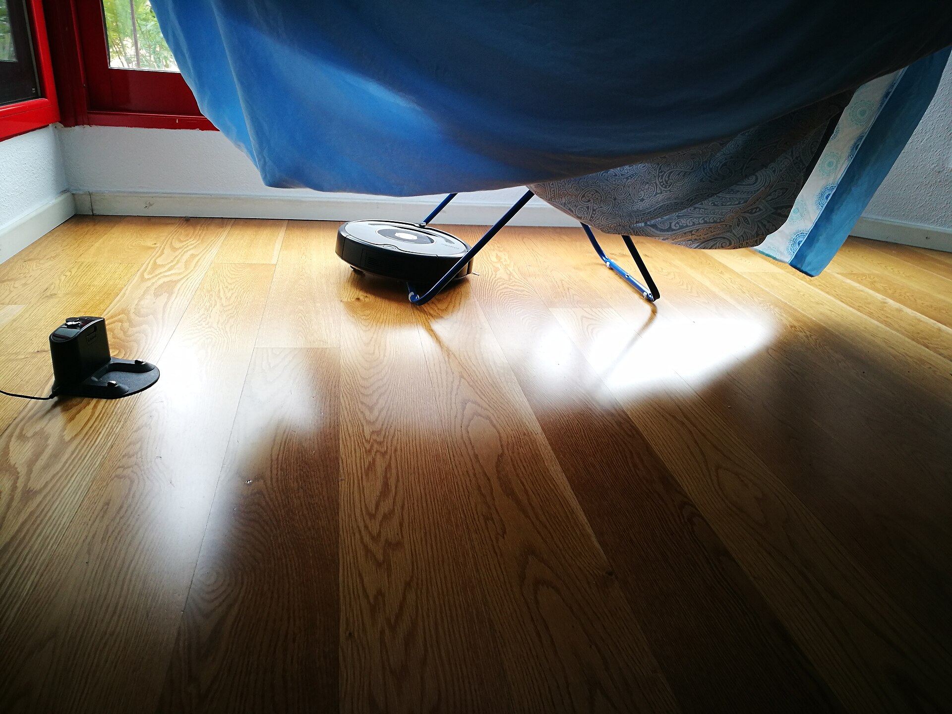 A round robot vacuum cleaner that has become stuck underneath a folding clothes dryer.