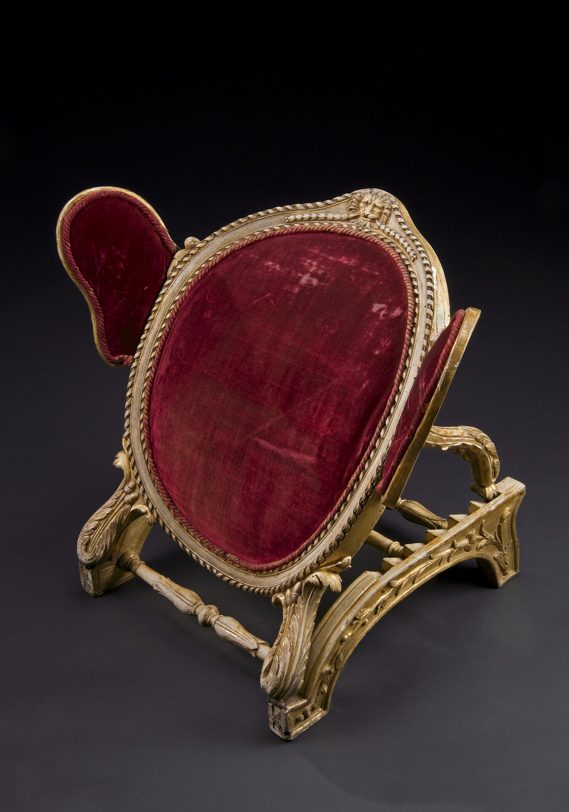 An eighteenth-century wooden adjustable bed rest with padded red velvet supports.