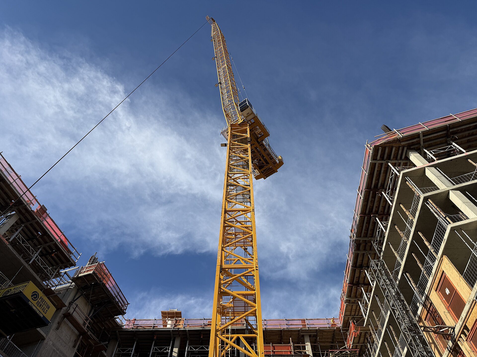 A yellow tower crane rising above a construction site against a blue sky.