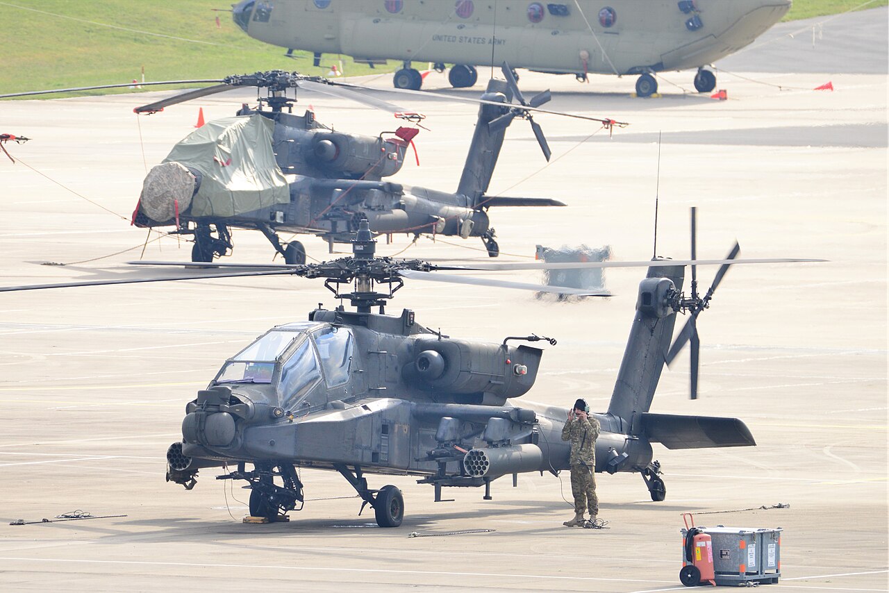 An AH-64 Apache helicopter on the ground, showing its main rotor on top and tail rotor at the back.