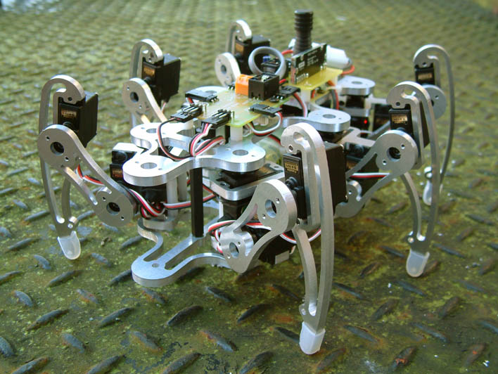 A six-legged hexapod walking robot with metal legs and servo motors, standing on a metal floor.